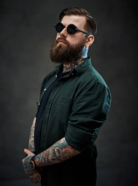 Ritratto di un ragazzo tatuato barbuto con camicia verde e occhiali da sole — Foto Stock