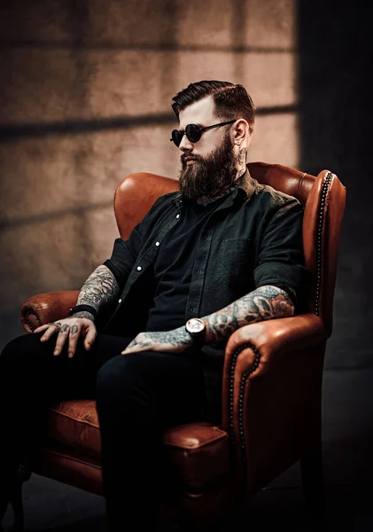 Cool bearded young man sitting on a vintage chair in studio — Stock Photo, Image