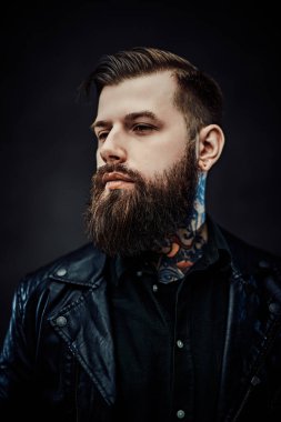 Deri ceket giyen, kendine güvenen, şık sakallı bir adamın yakın plan portresi.