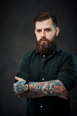 Koyu bir arka planda poz veren yakışıklı, dövmeli, şık saçlı bir adam.