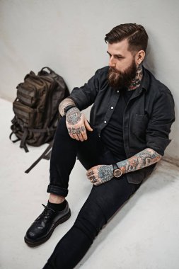 Sırt çantalı sakallı hippi stüdyoda yerde oturuyor.