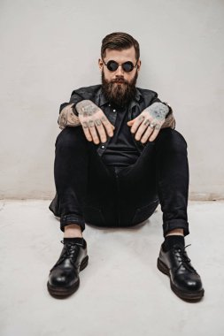 Güneş gözlüklü havalı sakallı hippi stüdyoda yerde oturuyor.