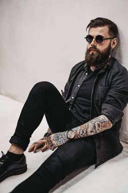 Güneş gözlüklü havalı sakallı hippi stüdyoda yerde oturuyor.