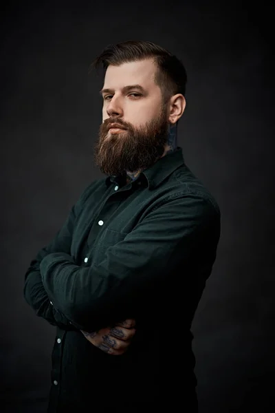 Portrait of a bearded young man posing posing with crossed hands and a confident look in studio — Stock Photo, Image