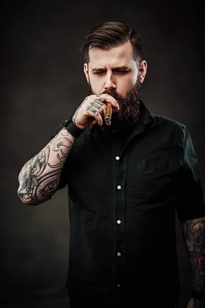 Studio portrait of a handsome tattooed hipster guy who smokes a cigar — Stock Photo, Image