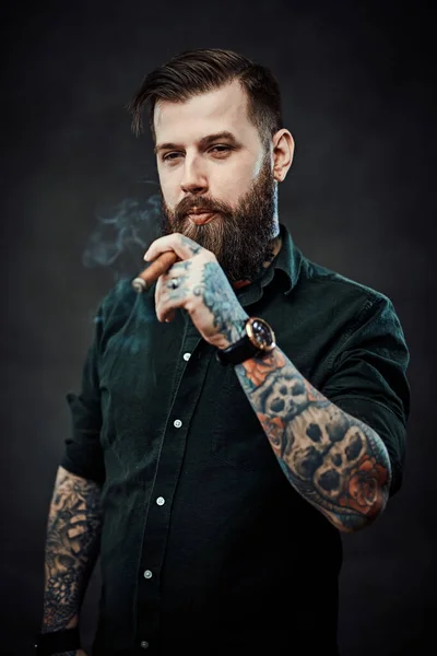 一个英俊的纹身嬉皮士抽雪茄的工作室肖像 — 图库照片