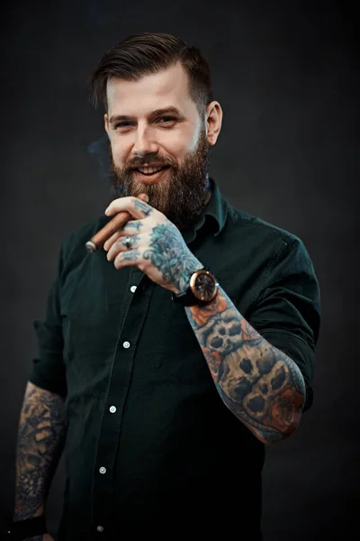 Studio portrait of a handsome tattooed hipster guy who smokes a cigar — Stock Photo, Image