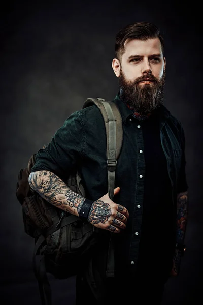 Portré egy hipszter fickóról hátizsákkal egy sötét stúdióban. — Stock Fotó