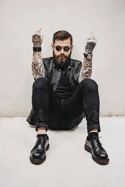 Жорстокий бородатий хлопець, що показує середній палець робить хуй вираження, сидячи на підлозі — стокове фото