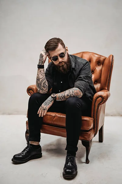 Cool bearded young man sitting on a vintage chair in a studio — Stock Photo, Image