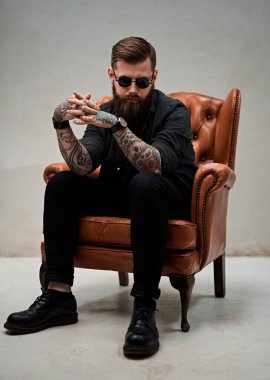 Stüdyoda eski bir sandalyede oturan havalı sakallı genç adam.