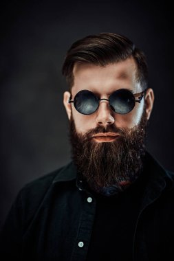 Koyu bir arka planda güneş gözlüklü havalı sakallı bir erkek portresi.