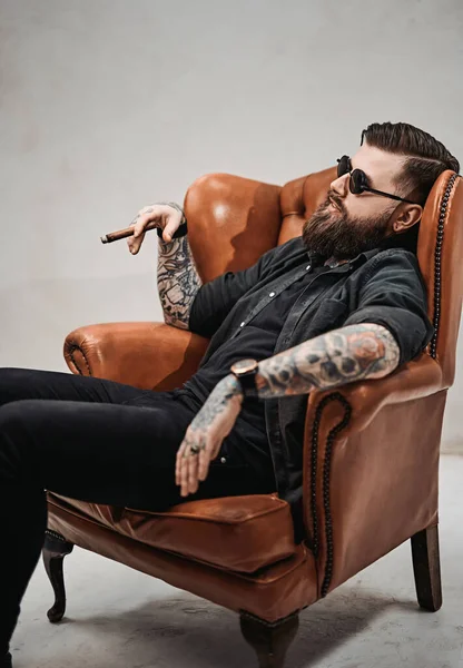Прохолодний бородатий чоловік курить сигару і розслабляється на старовинному стільці — стокове фото
