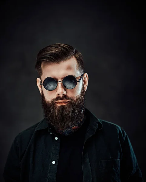 Retrato de un hombre barbudo fresco en gafas de sol sobre un fondo oscuro —  Fotos de Stock