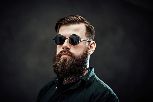 Retrato de un hombre barbudo fresco en gafas de sol sobre un fondo oscuro — Foto de Stock