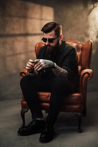 Cool bearded young man sitting on a vintage chair in studio — Stock Photo, Image