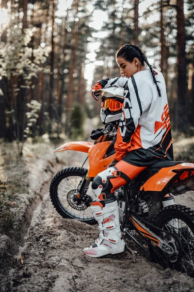 Bella giovane pilota donna in moto motocross su una scia di sabbia nel bosco — Foto Stock