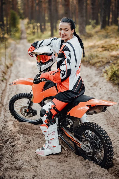 Feliz corredor femenino con traje de motocicleta sentado en su bicicleta fuera de la carretera en el bosque —  Fotos de Stock