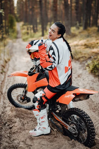 快乐的女赛车手穿着摩托车服坐在林子里的自行车道上 — 图库照片