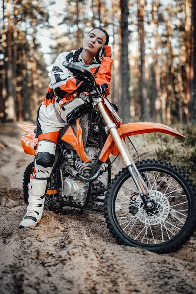 Bella giovane pilota donna in moto motocross su una scia di sabbia nel bosco — Foto Stock