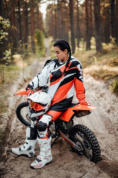 Hermosa hembra corredor sentada en su moto de motocross en un sendero de arena en el bosque — Foto de Stock