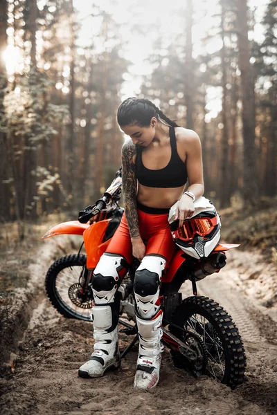 Kvinnlig racer bär motocross outfit med halvnaken bål sitter på sin cykel i skogen — Stockfoto