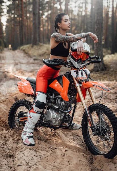 Corredor femenina con traje de motocross con torso semidesnudo sentada en su bicicleta en el bosque — Foto de Stock