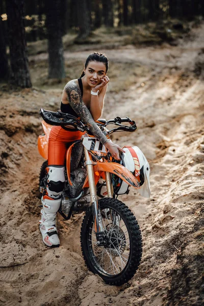 Motokros kıyafeti giyen, yarı çıplak gövdesiyle ormanda bisikletinin üstünde oturan bir kadın yarışçı. — Stok fotoğraf