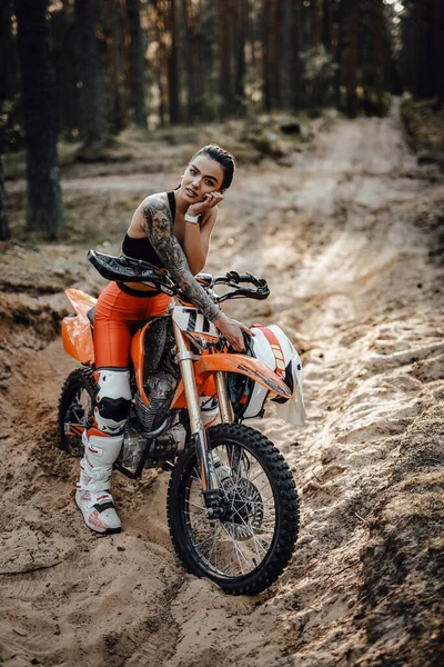 Femmina pilota indossa abito motocross con torso semi nudo seduto sulla sua moto nella foresta — Foto Stock