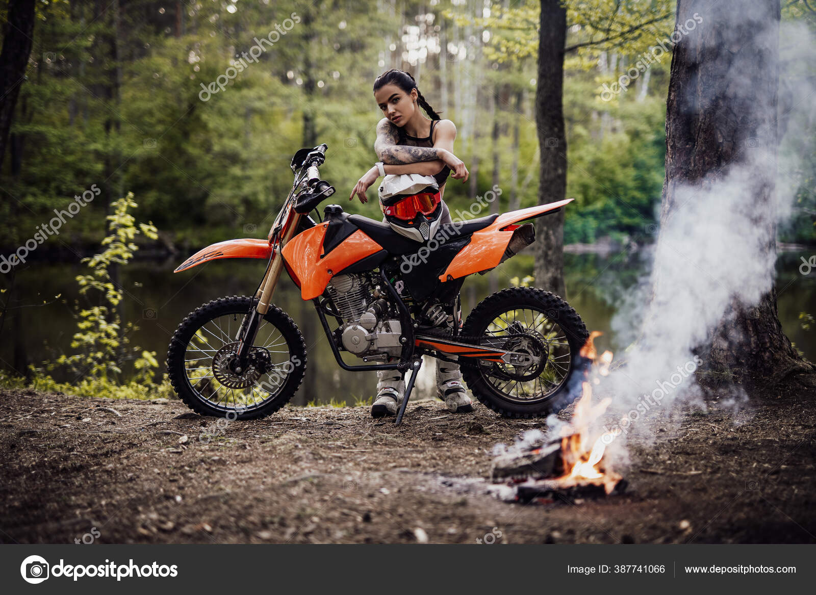 Encantadora joven corredor con traje de motocross con el torso semidesnudo  apoyado en su bicicleta y mirando una cámara al lado de la hoguera en el  bosque: fotografía de stock © fxquadro #