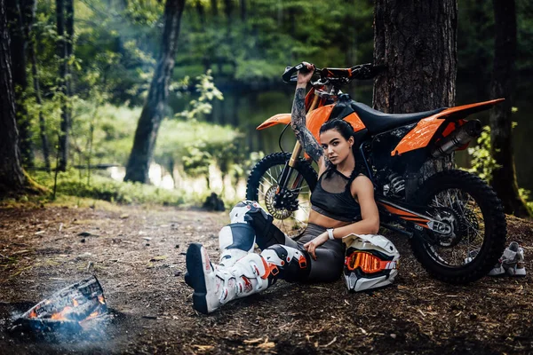 迷人的年轻女子赛车手身穿半裸躯干的越野赛服，坐在篝火边热身 — 图库照片