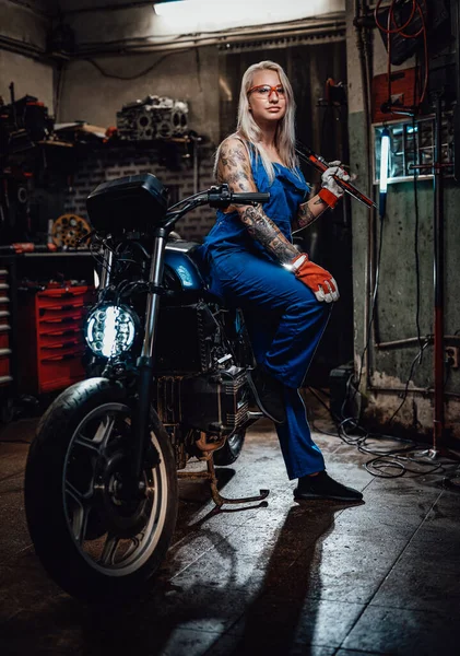 Samice vytetované mechanik v pracovní kombinéze držet velký klíč a pózování pro kameru v garáži — Stock fotografie