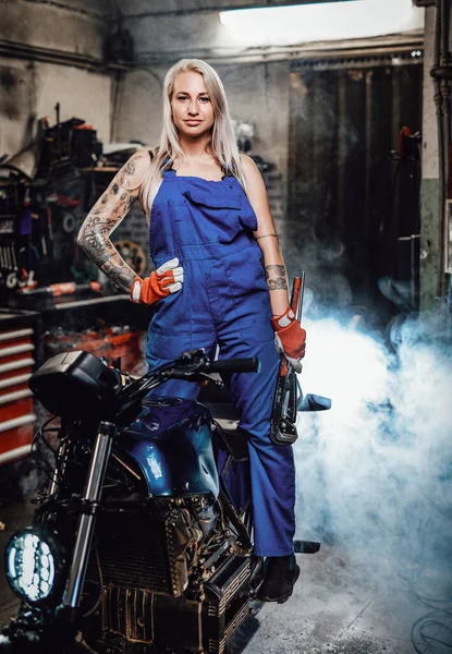 Bela mecânica feminina com as mãos tatuadas em macacões de trabalho posando para uma câmera na oficina — Fotografia de Stock
