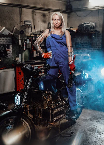 Όμορφη γυναίκα μηχανικός με τατουάζ τα χέρια στην εργασία φόρμες ποζάρουν για μια φωτογραφική μηχανή στο εργαστήριο — Φωτογραφία Αρχείου