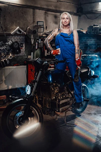 Όμορφη γυναίκα μηχανικός με τατουάζ τα χέρια στην εργασία φόρμες ποζάρουν για μια φωτογραφική μηχανή στο εργαστήριο — Φωτογραφία Αρχείου