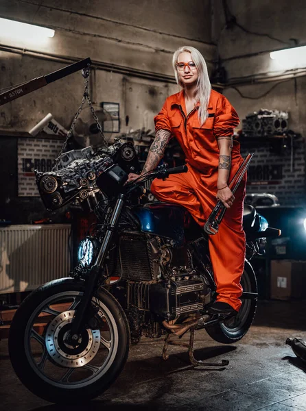 Bela mecânica feminina em macacão laranja segurar uma chave grande e posando para uma câmera na garagem — Fotografia de Stock