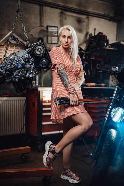 Όμορφη ξανθιά κοπέλα με τατουάζ σώμα φορώντας ροζ φόρεμα που ποζάρουν σε γκαράζ ή εργαστήριο — Φωτογραφία Αρχείου