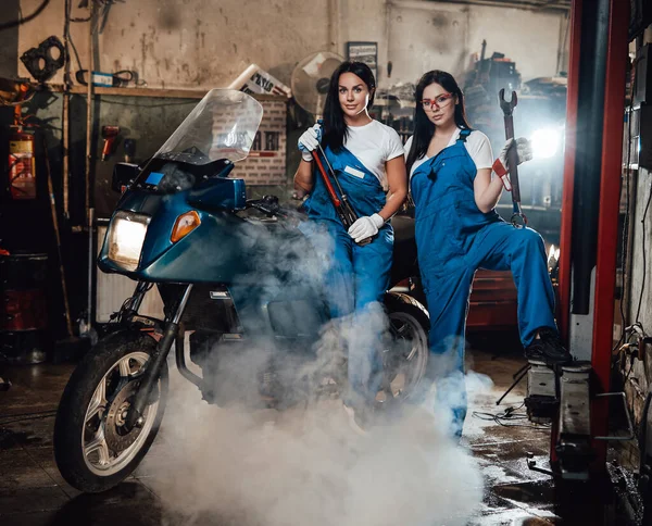 Dois mecânico feminino posando ao lado de um sportbike na garagem oficina autêntica cercada por fumaça — Fotografia de Stock