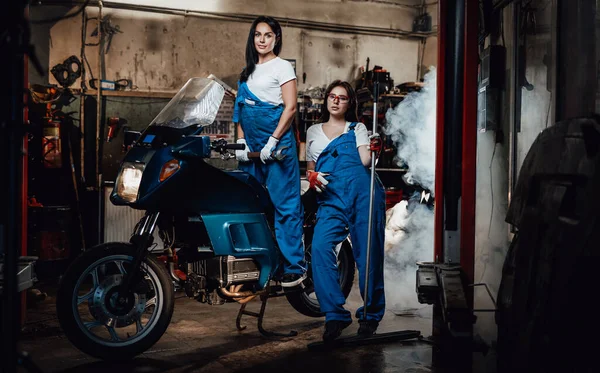 Dos mujeres mecánicas posando junto a una moto deportiva en un auténtico taller de garaje — Foto de Stock