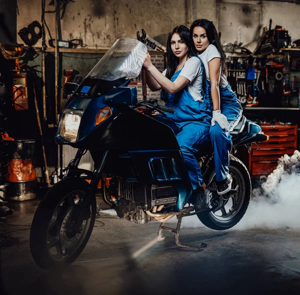 Dois mecânicos femininos sentados em sportbike na garagem oficina autêntica — Fotografia de Stock
