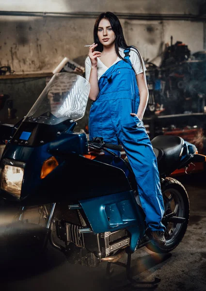 Samice mechanik relaxační kouření cigarety, zatímco stojí na sportovním kole v garáži nebo dílně — Stock fotografie