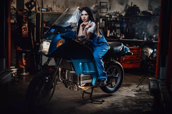 Linda morena mecânica feminina fumar um cigarro enquanto sentado em sportbike na garagem — Fotografia de Stock