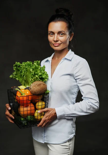 Retrato de una mujer feliz de mediana edad en delantal sostiene una canasta de verduras frescas y frutas — Foto de Stock