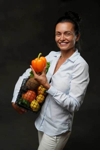 Donna di mezza età tiene un cesto di verdure fresche e frutta, sorridente e guardando su una macchina fotografica — Foto Stock