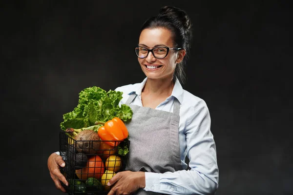 Önlüklü mutlu orta yaşlı bir kadının portresi bir sepet taze sebze ve meyve tutuyor. — Stok fotoğraf