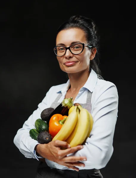 Linda agricultora de meia-idade em avental detém um monte de vegetais frescos e frutas — Fotografia de Stock