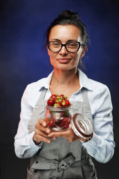 美しい中年女性は新鮮な赤いジューシーな果実を持つガラスを保持しています。暗い背景のスタジオ写真 — ストック写真