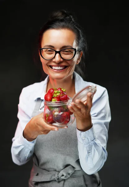 Krásná žena středního věku drží sklenici se zralou šťavnatou jahodou, usmívá se a dívá se do kamery — Stock fotografie