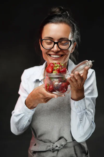 メガネの美しい女性は、ガラスの果物を保持し、新鮮なジューシーなイチゴの香りを吸い込みます — ストック写真
