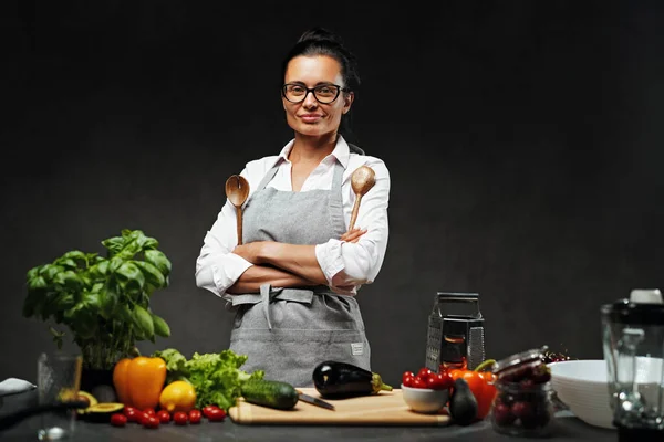 Chef feminino posando ao lado de uma mesa na cozinha — Fotografia de Stock